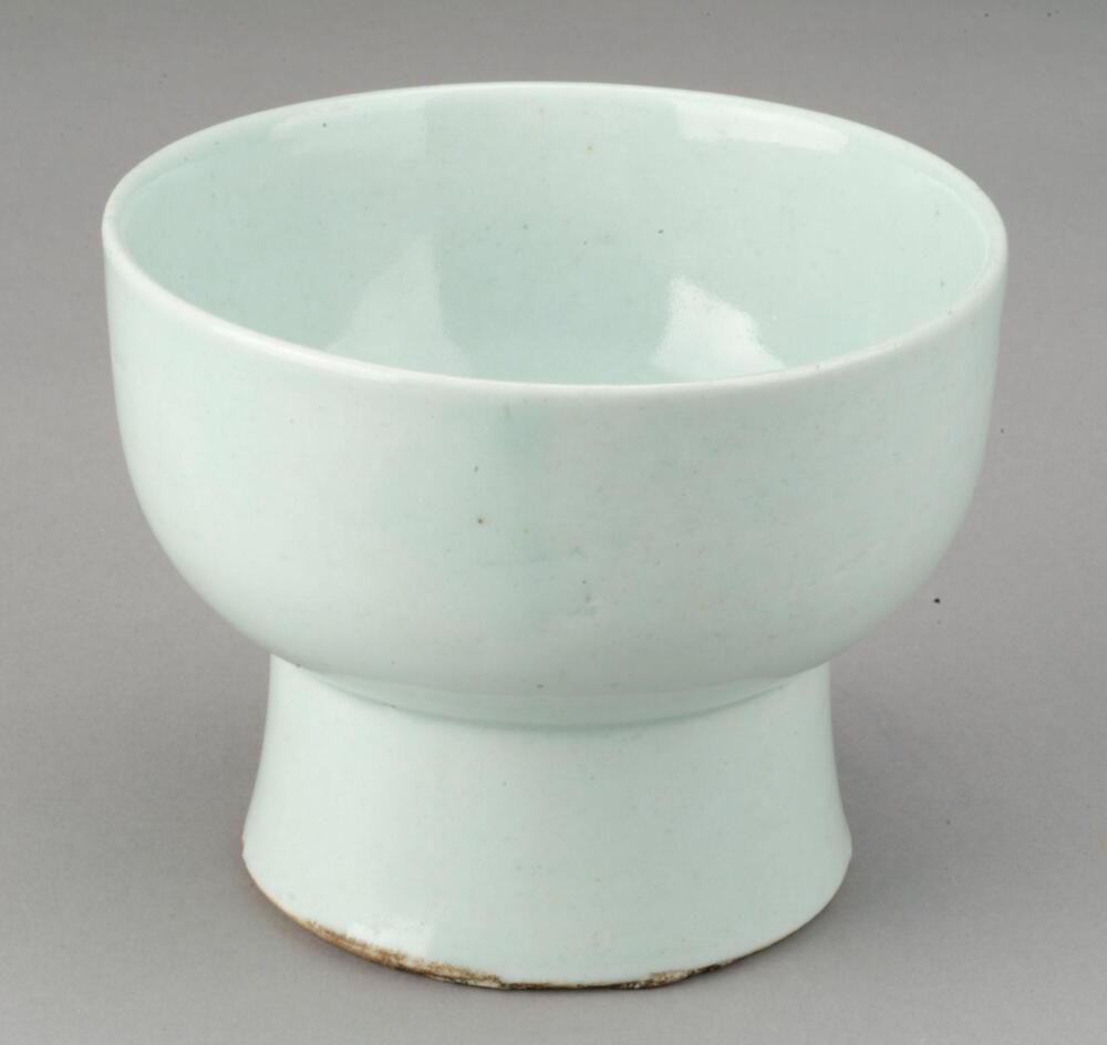This is a ritual bowl with a high foot. A same type of this bowl is found in the storeroom of Changdeokgung Palace. It was coated with the transparent glaze with pale blue tints. The glazed surface is impeccable. The qualities of the clay and glaze suggest that this bowl was produced at the kiln in Bunwon-ri, Gwangju-si, Gyeonggi-do in the late 19th century, the last official court kiln of the Joseon Dynasty.<br />
[Korean Collection, University of Michigan Museum of Art (2014) p.194]