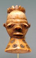 This small Pende ivory pendant (<em>ikhoko</em>) depicts a delicately carved male head. Stylistically, <em>ikhoko</em> bear many of the facial characteristics of anthropomorphic Pende <em>mbuya</em> masks, after which they have been modeled. In this particular example, an ovoid head rests atop a conical neck and features a spiked, crown-like coiffure, a large, bulbous forehead, a V-shaped brow, laterally protruding ears, heavily lidded and downcast eyes, an up-turned nose, a wide mouth, and a slightly pointed chin. Circular motifs decorate the top of the forehead and the neck. The pendant also possesses a pale yellow patina, possibly from contact with tukula powder.