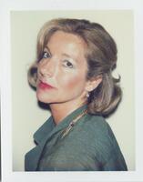 A bust-length portrait of a woman. She is wearing a green shirt, a necklace, earrings and red lipstick. She has straight, chin-length blonde hair that is pinned back. She stands at an angle and looks into the camera lens.