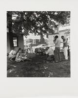 Black and white image of a group of peple outdoors. Two men are taking photographs of four women and two babies while two other men watch the rest of the group.