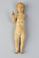 A nude, standing child figure with the right hand raised to chin-level. The forefinger and middle finger are raised and the thumb is out. 