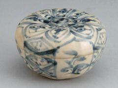 A melon-shaped stoneware box with a lid, the shape slightly faceted on the sides and the lid concave to a disk-shape center. The box is decorated with freehand floral and geometric designs in blue cobalt pigment, and then a whitish glaze was applied to the whole.