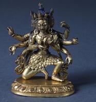 A miniature figure of a tantric goddess, very finely cast by the cire perdue (lost wax) method. The goddess is shown seated in lalitasana pose ("royal ease," one knee bent and the other relaxes) on a lotus dais, which is separately cast. She has 8 arms which are in variants of vitarka mudra (the gesture of teaching).  She has three heads, with the two lateral heads seen here as partial profiles; each wears the five-petal tiara of Tibetan Buddhist ritual. Her skirt is unusual, looking to be made of leaves, instead of the usual dhoti. Her hair is painted blue and her lips red.