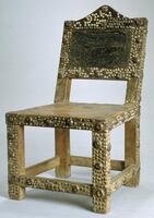 This wooden chair has a square, leather covered seat and four legs. The back of the chair also has a leather covering. Much of the chair is decorated with metal tacks.
