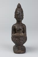 Kneeling female figure on a rectangular base, holding a bowl decorated with a human face. The bowl is supported by a short cylinder. The figure has bracelets on each wrist and chevron-shaped marks on each arm. The hair is in a comb-like shape, decorated with vertical grooves. 