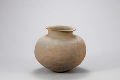 Jar with a round base, short neck and flaring mouth. Fabric imprints and gently indented lines stretch across the round body of the jar.<br />
<br />
This is a blue-gray, round-bottomed, high-fired stoneware jar with a short neck. Its neck curves outwards towards a widely flared mouth. The edge of the rim is slightly round, and the inner surface of the mouth is flattened. The inner and outer surfaces of the neck show traces of rotation and water smoothing. The body is widest at its upper-middle section, while its surface has been decorated with shallow horizontal lines after the rendering of a dense lattice design. The upper part of the vessel shows traces of an erased paddled pattern, and there are cracks on the inside of the base.<br />
[Korean Collection, University of Michigan Museum of Art (2017) p. 46]<br />
<br />
&nbsp;