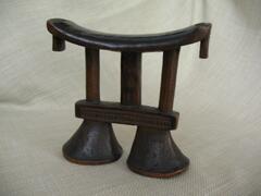 Zimbabwe, with geometric forms.<br />
Headrests are small furnishings, typically sculpted from wood. They frequently have a concave platform supported by legs, though the platform can also be flat and/or be supported by a central post that may be connected to a broad base. The platform may be cushioned to provide comfort for the owner&rsquo;s head, and many headrests feature complex ornamentation and sculptural details. Headrests share some of the same motifs and associations with stools, as they are constructed similarly and used for similar purposes.