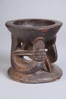 Small bowl supported by two fish on a circular base. The two fish are curved so that the head, tail, and one fin support the bowl while the middle of the body rests on the base. The other fin connects the fish&#39;s tail to the head. The edge of the bowl and the base are decorated with incised diagonal marks.&nbsp;
