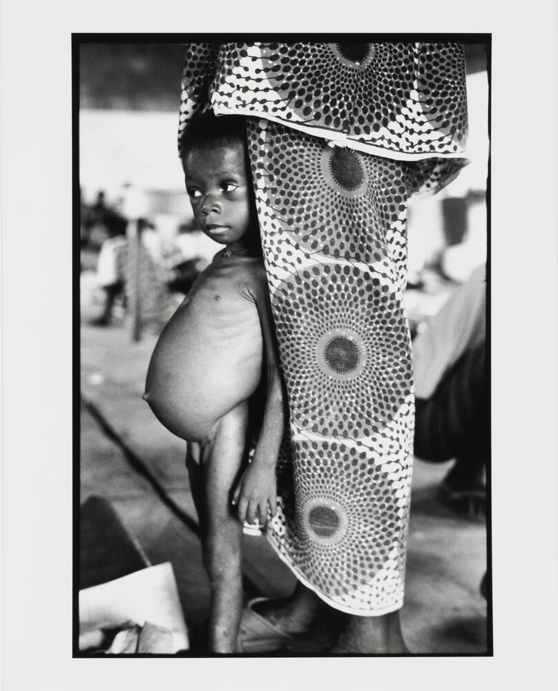 Image of a young child leaning against his mother, who is clothed in Dutch wax print.