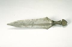 The blade of this sword has two slight, triangular protrusions on each edge. On one side of the blade are closely placed incisions running the length of the blade. The wooden handle is wrapped in wire. 