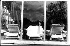 Photograph of a series of three beach lounge chairs in a windowed room. A single foot rests at the top of the center chair. 