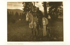 This is a photograph of a horse and rider. Both wear patterned, geometric costume and are framed by an wooded landscape.