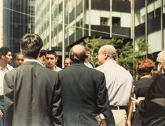 Image of a group of men, 3 in the foreground with their backs to the viewer. Behind them are more men facing the viewer.