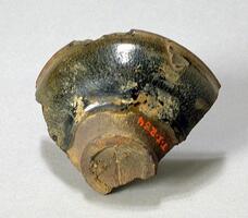 A fragment of a Jian Ware bowl&nbsp;with mottled black-brown glaze. It is on a short footing and a everted rim.