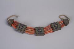 a bracelet consisting of horizontal orange beads and metal squares.  The metal squares are painted with a blue and green design.