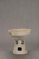 A ceramic ridged bowl with a tall, trapered cylindrical stand.  The base is detailed with staggered square cut-outs.