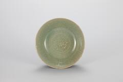 <p>This dish is decorated with a mold-impressed single chrysanthemum design at the center of its inner base. Glaze has been applied rather thickly, but is well fused and clear to form a crystalline surface tinged with blue. The glaze on the outside of the base has been partially oxidized, producing a brown hue. Crackles are spread throughout the surface. The inner walls are decorated with low relief of ten chrysanthemum spray designs. The base is at and has no foot, while traces of quartzite supports remain in three places.<br />
[<em>Korean Collection, University of Michigan Museum of Art </em>(2014) p.113]</p>
<br />
Dish is decorated with a mold-impressed single chrysanthemum design at the center of the base. Glaze has been applied thickly, forming a crystalline surface tinged with blue. The outside glaze has been partially oxidized, turning it slightly brown. The innter walls are decorated with ten chrysanthemum spray designs. Traces of quartzite supports can be seen on the bottom of the dish.