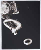Square black and white photograph depicting three smoke rings that float in the air against a black backdrop. The rings appear in a diagonal pattern, one in the lower left corner, one in the center and one in the upper right corner. The ring in the lower left hand corner appears to be more complete, while the other two are more abstract.