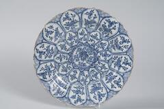 A blue and white charger that has two circular registers of reserve panels. The reserves have images of flowers within them. In the very center of the charger is a group of flowers.