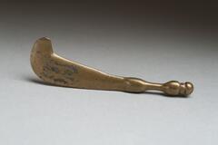 Gold-weight in the shape of a wide, flat blade with a curved hook at one end and a handle in the form of two balls connected by a narrow rod with a small ball the end. 