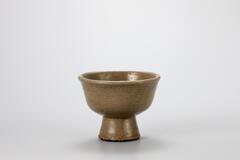 A tall stoneware bowl with a short, tapered cylindrical base. The bowl itself curves into a flat bottom where it meets the foot-base.<br />
<br />
The high iron content in the clay and glaze of this bowl produces a green-brown colour. In the Honam region (southwestern region including Jeollabuk-do and Jeollanam-do), the potters produced many vessels with celadon clay in the typical shapes of the white porcelain, thus resulting in the colors that resembles that of green celadon. This bowl is green-brown in color but has transparent glaze, giving it a very shiny surface. The entire foot was glazed, while there are eight sand spur marks on the foot rim. It was slightly deformed in the kiln, with the result the rim is not completely horizontal.<br />
[Korean Collection, University of Michigan Museum of Art (2014) p.195]