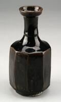 This brownish black bottle was made from porcelain clay coated in brownish-black glaze. The high-iron content of the glaze has given it a black shade. Sand has been removed from the clay, giving it a smooth texture. Coarse sand spurs were used during firing. The glaze is well fused and the surface is glossy. It remains intact and undamaged.<br />
[Korean Collection, University of Michigan Museum of Art (2014) p.212]
