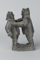 Two men carved from the same piece of stone. One man grasps the other man&#39;s arm. Both are wearing hooded coats.&nbsp;