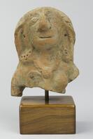 A bust with a prominent, raised face and nose, large eyes, earrings with dotted decorative markings, and a crest of hair, with vertical slashes. There is a necklace with a circular centerpiece. The right arm bends downwards and the left is severed at the shoulder.