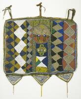 Cloth panel bound in leather with multi-colored beadwork. There are three evenly spaced leather ties across the top, while the bottom has three small, triangular panels attached, each with two strings of beads hanging down. The center of the panel has a face with an interlace pattern below. The rest of the panel has patterns of zig-zags and diamonds in various colors. 