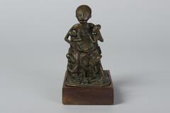 Seated figure holding two smaller figures with three more smaller figures in front, all made from a single piece of brass.&nbsp;