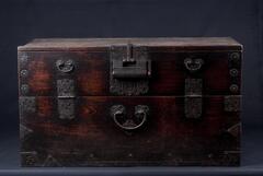 All parts of this chest, including the back, were made from solid zelkova planks, a luxury wood related to elm but with a more pronounced grain. This specimen has escaped aggressive cleaning with modern compounds and retains its original patina. The dovetail joints between the lower front panel and sides and the back and side panels are superbly wrought. The iron lock plate in the middle of the front is fashioned into an auspicious character, bok (good fortune). The rectangular iron hinges and square supporting corner brackets are fashioned into Buddhist swastika patterns. The four arms of each swastika radiate out from the center like the spokes of a wheel, symbolizing the rotation of the universe around the cosmic Buddha.<br />
<br />
This chest was kept in a lady&rsquo;s quarter (<em>anbang</em> ) to store clothes. Marks left on the inner surface indicate that the chest once contained a shelf. The side panels, back panel, and bottom panel were joined by finger joints, while the side panels and top plate 