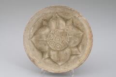A small, shallow stoneware bowl with flaring sides and a flat rim.  The interior is molded with an eight petal lotus flower, and it is covered in a pale gray-green celadon glaze. 