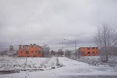 Two orange buildings on snow-covered ground on either side of an unplowed road.&nbsp;