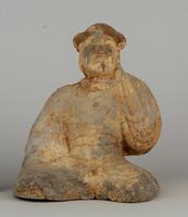 A grey earthenware figure of a man, seated with legs crossed, wearing a full belted robe with wide banded sleeves and a cap on his head.  His right hand is on his lap while the left hand is held cupping his ear.  It is covered in traces of slip and polychrome mineral paint.