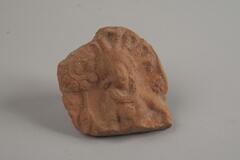 A piece of Indian terracotta fragment which shows a upper top of the body of a female figure, who is holding a scepter in her right hand. The female figure has a huge hair ornament on her head.