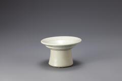 A tall glazed and speckled white-blue porcelain offering dish for an altar. The base is a wide, slightly tapered cylinder. The dish a the top is quite wide and shallow until it reaches the point of the base, where there is a deep hole in the cylinder of the base.<br />
<br />
This is a hard-paste cup stand with a glossy surface. It is a high-grade object and was produced at a kiln in Bunwonri, Gwangju-si, Gyeonggi-do. There are fine cracks in one side of its foot.<br />
[Korean Collection, University of Michigan Museum of Art (2014) p.201]