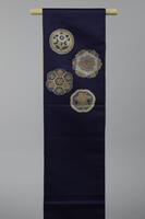 <p>Thin dark blue fukuro (single-sided) Obi with interwoven white, beige, orange, bronze, and light blue stylized floral motifs arranged within various circles and wreath-like shapes.</p>

