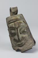 Bell or gong in the form of a rectangular human head. On each side there is an image of a woman surrounded by what may be snakes. At the top of the object is an open loop. The bottom of the object is open with some cracks along the bottom edges.