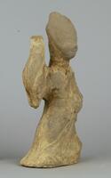 A gray earthenware figure of a female wearing a long flowing robe with wide sleeves, and elaborately dressed hair. Her right hand is held high while the left hand is held over her hip. There are traces of slip and polychrome mineral pigment. 