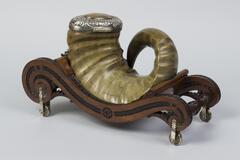 Ram&#39;s horn mull with a silver hinged lid and shield-shaped plaque on the side. The top and sides of the lid have a raised foliage design and an orange-toned chalcedony in the center. The wooden cart rests on silver wheels and has a green velvet bed and silver brace shaped to support the mull.