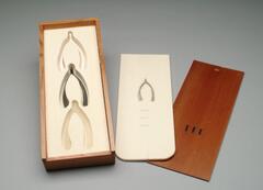 A rectangular wooden box containing ceramic, rubber, and bronze wishbones encased in felt. A lithographed felt card rests on top of the wishbones. The text on the felt card reads: Wish #1 Wish # 2 Wish #3. The box top is engraved with "III" on the front. 