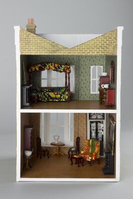 Dollhouse replica of a two-storey Victorian-style flat in the East End of London. The façade is red brick with white molding. The upper storey has two tall windows that face onto the street; the door into the flat is on the left, and to the right of it is a large bay window. The split-level interior holds a bedroom and parlor, both of which are decorated with wallpaper and furnishings, including cabinets, chairs, tables, fireplaces, and a canopy bed. Reproductions of paintings by Shonibare and Jean-Honoré Fragonard hang on the walls. A seal on the right-facing outside wall reads: “Yinka Shonibare, artist, lives here.”<br /><br />
First Floor: Reproduction of Diary of a Victorian Dandy: 14:00 Hours (1998) by Yinka Shonibare; Cabinet with shelves and books; wing chair with footstool; large bureau; fireplace; round table; side table; two chairs; bowl and cup;<br /><br />
Second Floor: Canopy bed; mirror; small bureau; reproduction of The Swing (1767) by Jean-Honore Fragonard; fireplace; chair; washstand with pit