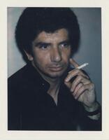A bust-length portrait of a man. He wears a black shirt and holds a cigarette in his hand. 