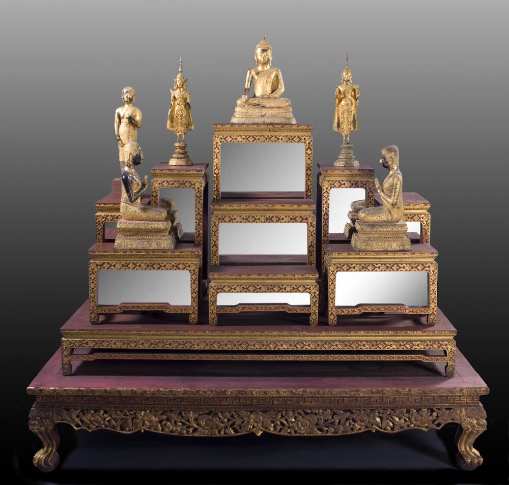 Gilt and lacquered wooden table of ten-piece altar set. Not including the base, the set is designed in three rows, which simultaneously recede from the viewer and increase in height, culminating in one central table that rises above the rest allocated for a statue of the Buddha. Each table is carved along the edges in stylized floral and leaf patterns coated with gold gilt. The wood surfaces of the tables are coated in red lacquer, and with the exclusion of the short, wide base, each table in the set includes a mirror designed to face the viewer.