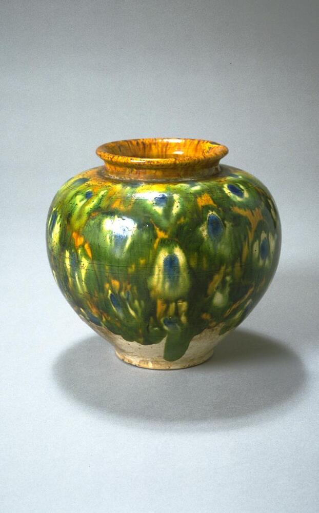 An earthenware globular jar with high wide shoulder, tapering to a narrow base. The jar hasa wide, short neck with everted rim, and the rim is covered in an amber glaze, the body covered in an amber, green, cream, and blue peacock-feather pattern, stopping short high above the base.