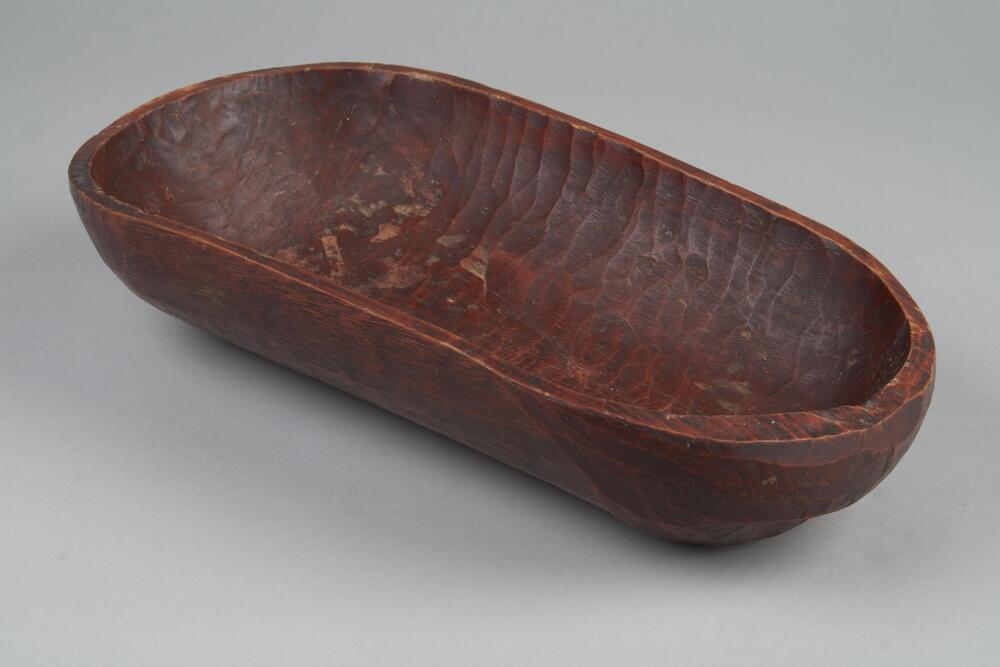 A large and rectangularly shaped carved wooden bowl. Two of the sides of the bowl are closer to being flat surfaces than round.<br />
<br />
These large bowls (<em>hamji</em>) were made by carving out large, single pieces of wood. Notches or handles have been carved out on two opposite sides of the outer walls, making them easy to carry. Round hamji bowls were sometimes carved on a turning lathe, but those with notches could be made by carving out single lengths of wood with an adz. These bowls were used in towns and the countryside alike. Affluent households would possess sets of large, medium-sized, and small bowls with notches piled up together. When grinding mung beans, beans, or red beans, such bowls are placed below a grindstone supported by a tripod.
<p>[Korean Collection, University of Michigan Museum of Art (2017) p. 274]</p>
