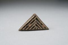 Gold-weight in the shape of a flat triangle with a pattern of raised, nested chevrons. 