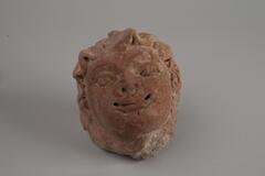 Indian terracotta head figure with opened eyes, nose and smiling mouth.