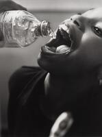 Black and white image of a child with water being poured into their mouth by someone out of view.&nbsp;