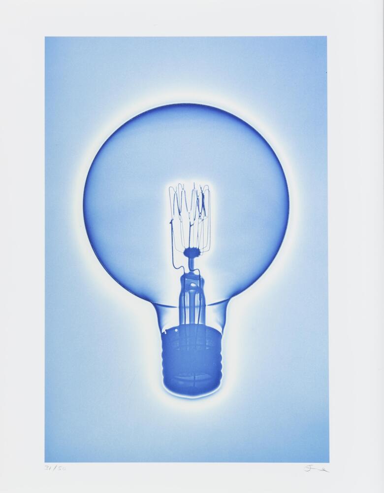 A color photograph featuring a light bulb. The bulb is surrounded by white and the base and outline of the bulb are dark blue. The background of the image is a pale blue.
